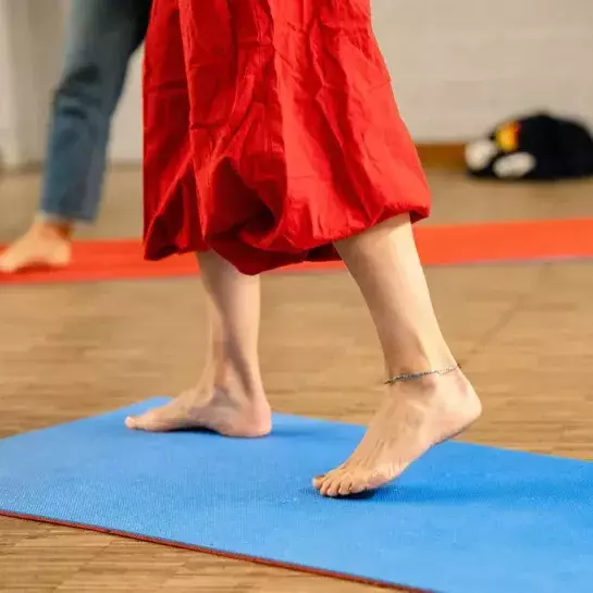 Benen van een persoon met een rode jurk die op een yoga-matje staat. 