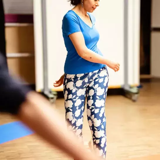 Een vrouw staat op een yogamat en beweegt met haar armen. 